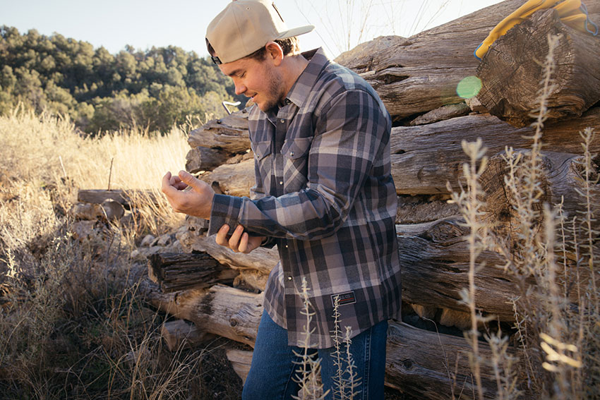 Man wearing plaid shirt and cap outdoors, showcasing workwear brands.